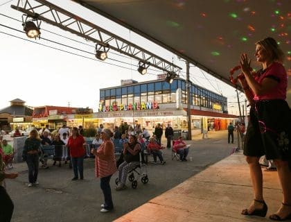 Female singer wearing a pink top and black skirt performing in front of a crowd on a stage across from Joe's Playland by the beach in Salisbury MA