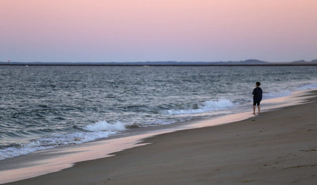 Silhouette of a person standing in the sand watching the beautiful pink and blue sunset over the water at Salisbury Beach in Salisbury MA