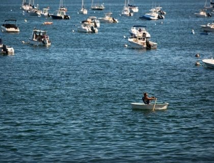 Woman with sunglasses canoeing by boats and moorings in the middle of the blue water in Swampscott MA