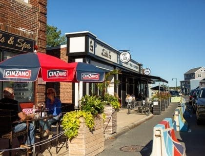 View of patrons enjoying the sun eating at the outdoor tables of the beachside restaurants located on Humphrey Street in Swampscott MA
