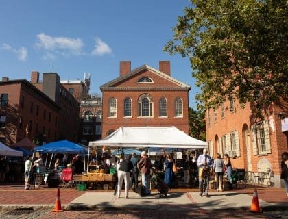 View of the Farmer's Market filled with shoppers in front of the Old Town Hall at Derby Square in Salem MA