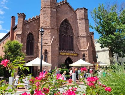 The Salem Witch Museum on a bright sunny day, with pink flowers in the foreground.