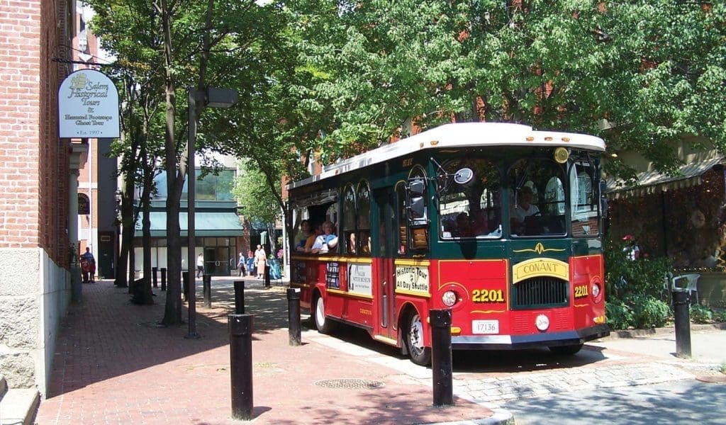 A trolley for tourists coming down the street next to the Salem Historical Society on a beautiful clear day in Salem MA