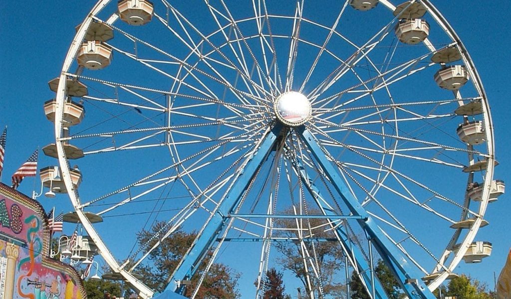 View of a crowd in front of the ferris wheel on a clear blue sky day at Topsfield Fair in Topsfield MA