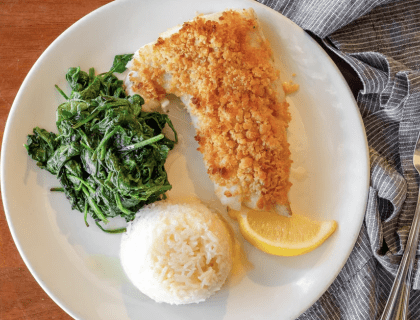 A fresh dish of baked haddock with cooked spinach, white rice, and a lemon wedge on a white plate from Turner's Seafood in Salem, MA.