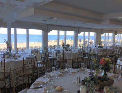 An elegant event setting with round tables at sunset in the Atlantic Ocean Room at the Elks at Bass Rocks in Gloucester, MA.