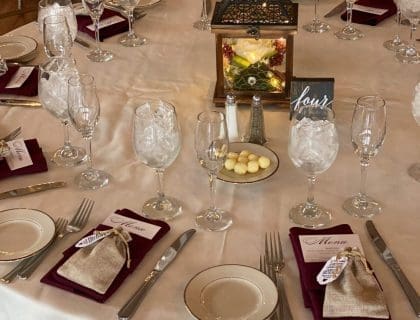 A closeup of an elegantly set table with a white table cloth and warmly lit lantern centerpiece in the Atlantic Ocean Room at the Elks at Bass Rocks in Gloucester, MA.