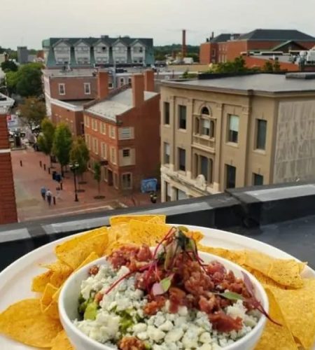 A full plate of tortilla chips with a bowl of guacamole dip in the center on a ledge overlooking the town of Salem MA.