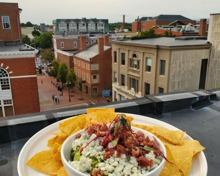 A full plate of tortilla chips with a bowl of guacamole dip in the center on a ledge overlooking the town of Salem MA.