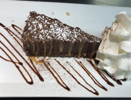 A wedge of chocolate torte dessert with a drizzle of chocolate syrup underneath and a scoop of vanilla icecream.