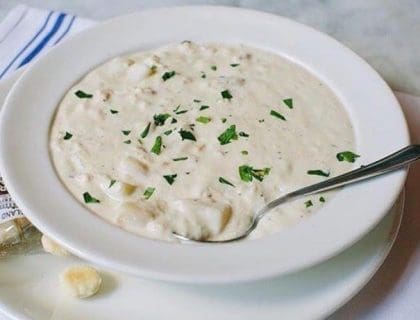 Freshly prepared New England Clam Chowder from Turner's Seafood in Salem, MA in a white bowl with a silver spoon in the chowder and oyster crackers on the saucer.
