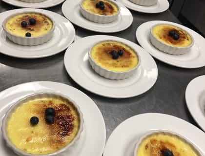 A display of 13 freshly made creme brulee desserts on a silver table in the kitchen of Turner's Seafood in Salem, MA.