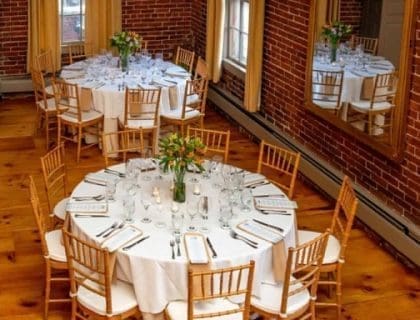2 elegantly set round tables in the warmly lit loft at Turner's Seafood in Salem, MA.