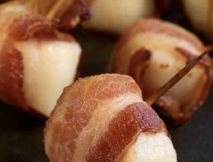 A close up bacon wrapped scallops on a wooden skewer.